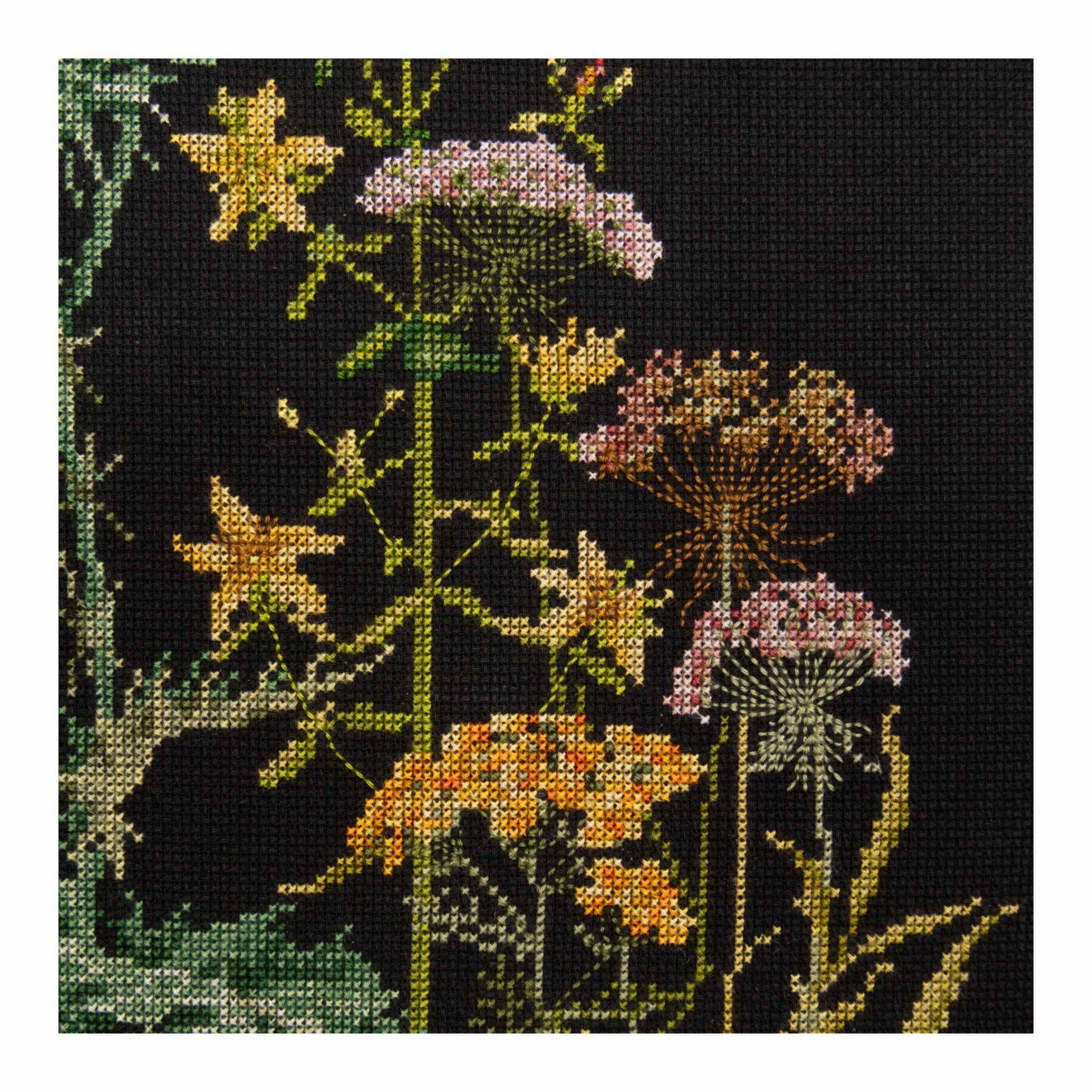 Cross-stitched floral design on black fabric with yellow, pink, and green flowers.