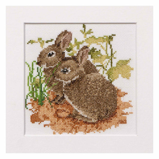Cross-stitched design of two bunnies in a natural setting with greenery.