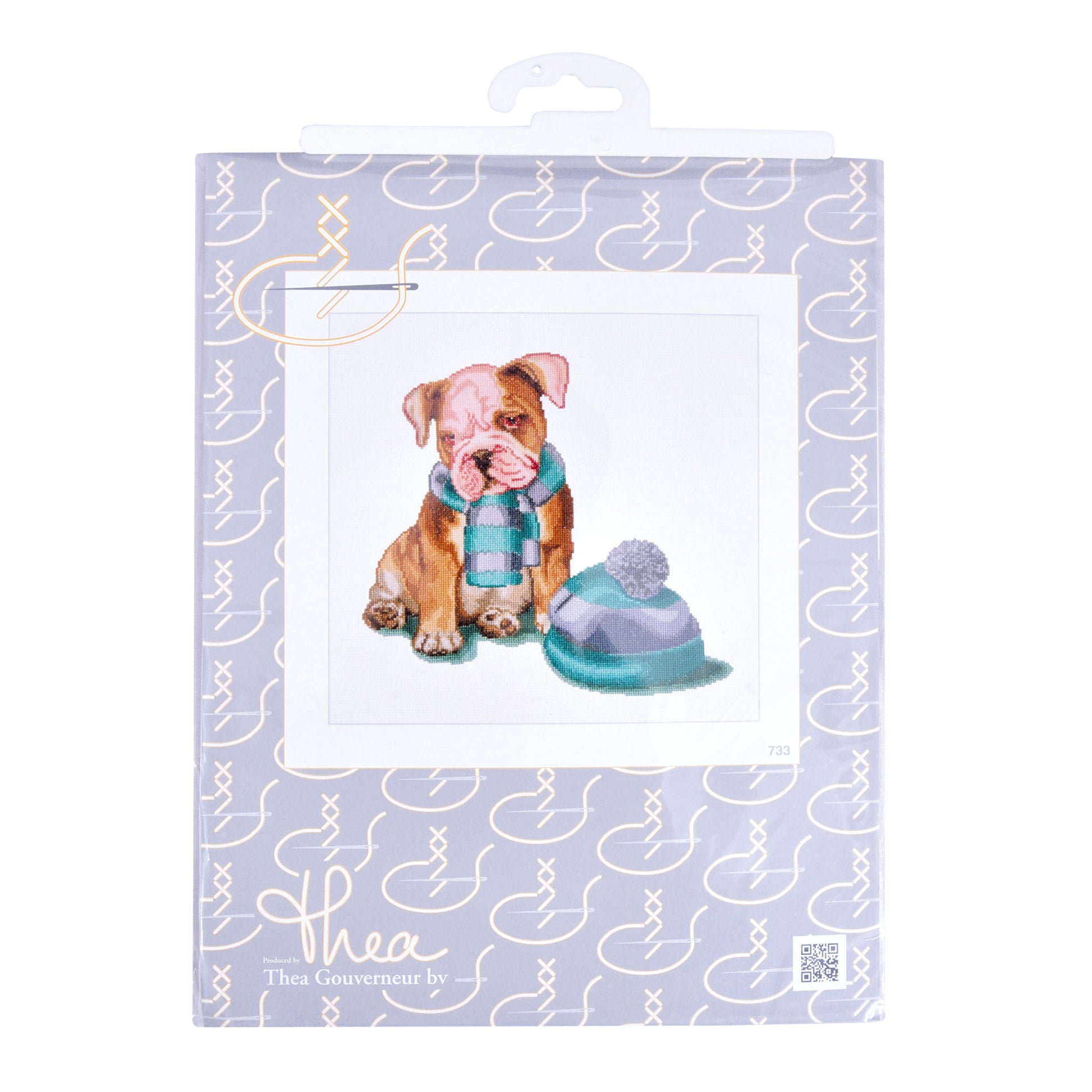 Cross stitch packaging with a dog illustration and decorative elements on a light purple background.