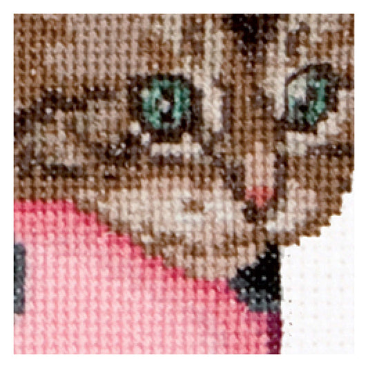 Close-up of a cross-stitched cat with green eyes on fabric.