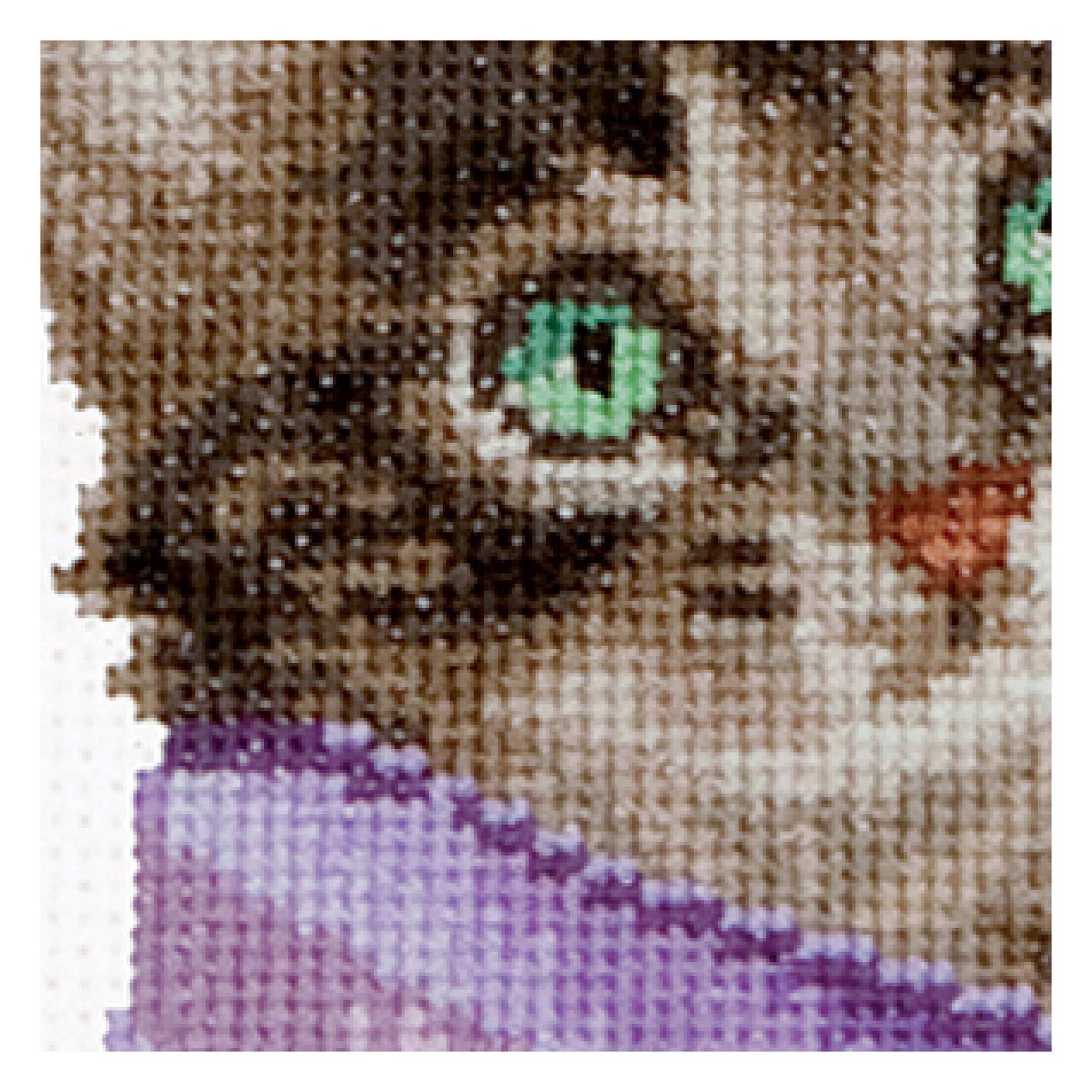Close-up of a cross-stitched piece depicting a cat's face with green eyes.
