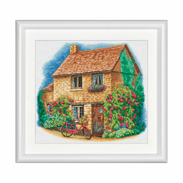 cross stitch design of a quaint cottage with a bicycle in front, surrounded by flowers and plants.