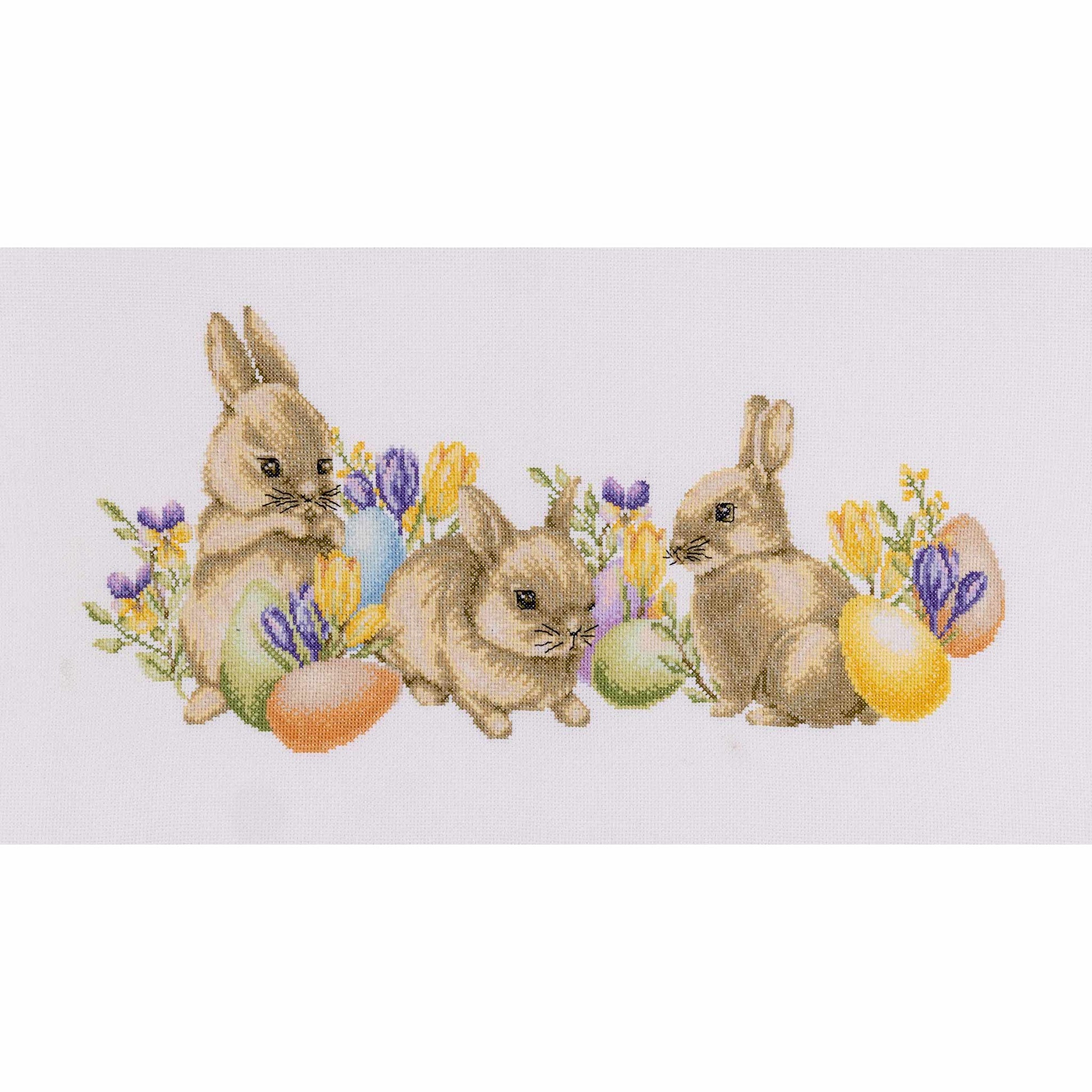 Cross-stitched design of three bunnies with Easter eggs and flowers on a white background