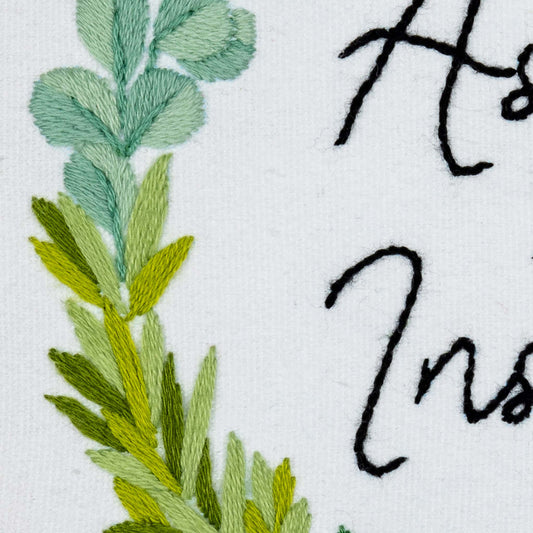 Embroidered green leaves and black text on a white background