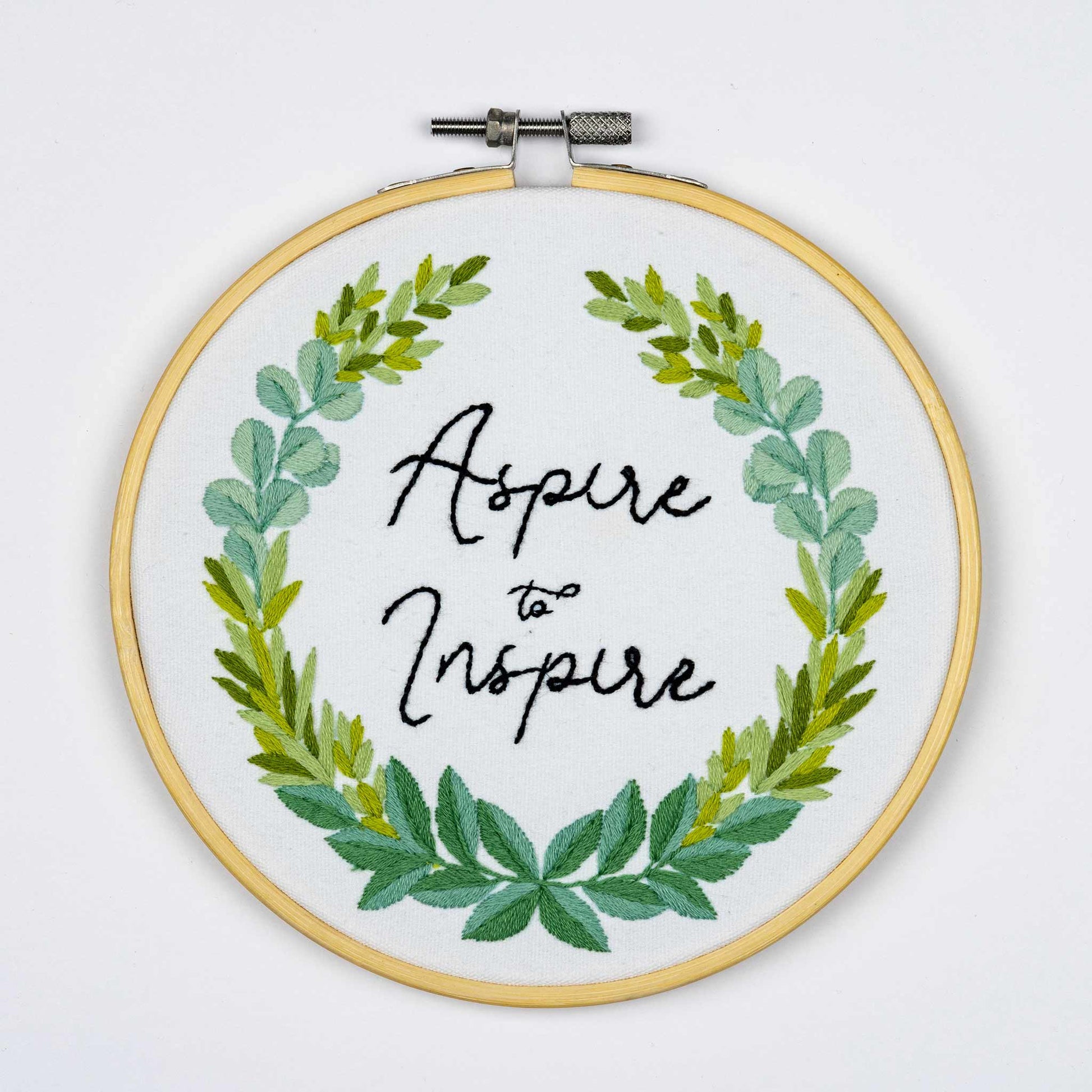 Embroidery on a hoop with green leaf design and 'Aspire to Inspire' text on a white background