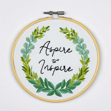 Embroidery on a hoop with green leaf design and 'Aspire to Inspire' text on a white background