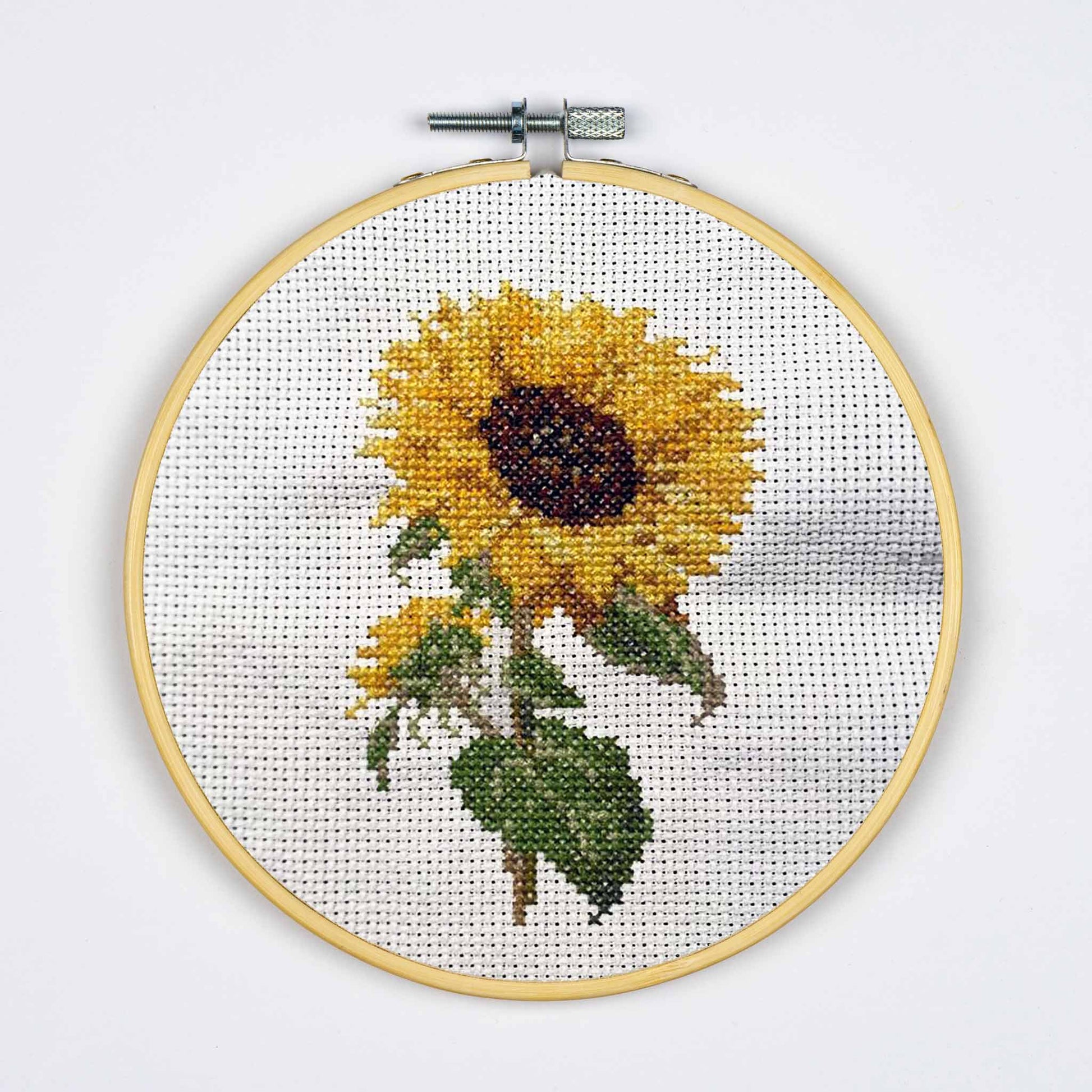 Cross-stitched sunflower in a wooden hoop on a white background