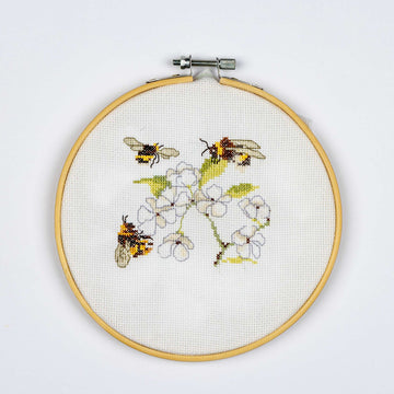 Embroidery hoop with cross-stitched design of bees and flowers on a white background