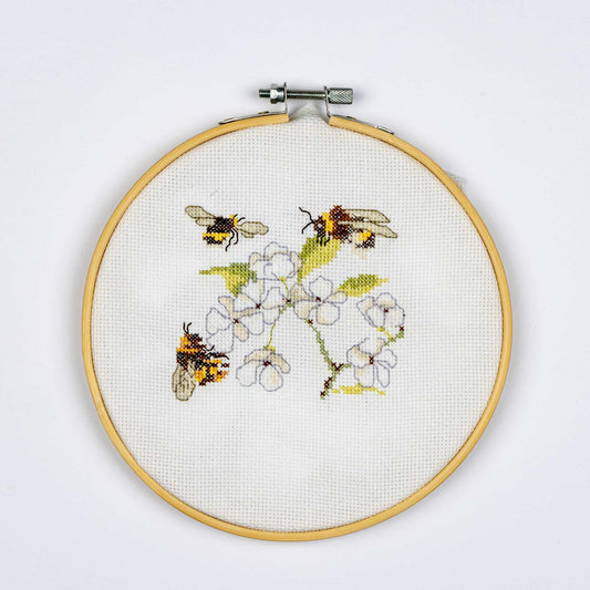 Embroidery hoop with cross-stitched design of bees and flowers on a white background