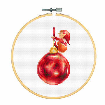 Cross-stitching hoop with a red Christmas ornament and elf design on white fabric.